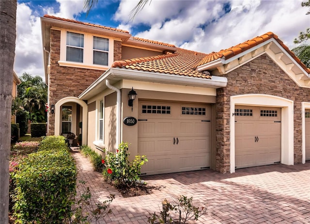 view of front of property with an attached garage, stone siding, decorative driveway, and stucco siding