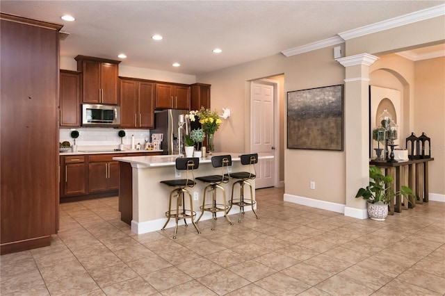 kitchen featuring a center island, light countertops, appliances with stainless steel finishes, ornamental molding, and a kitchen breakfast bar