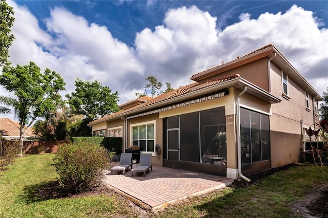 rear view of house featuring a sunroom, stucco siding, a patio, and a yard