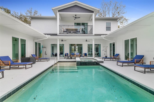 back of property with ceiling fan, a pool with connected hot tub, a patio area, and a balcony