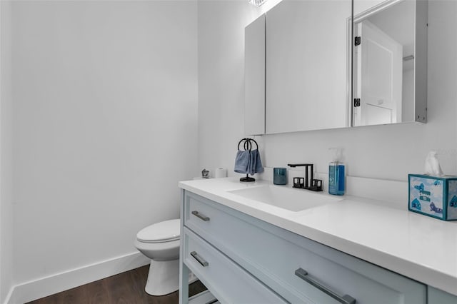 half bathroom with toilet, wood finished floors, vanity, and baseboards