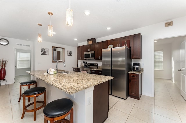 kitchen featuring light tile patterned floors, a sink, a kitchen breakfast bar, appliances with stainless steel finishes, and pendant lighting