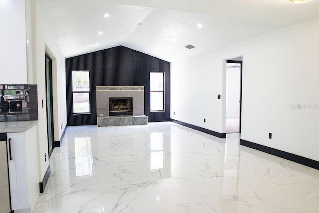 unfurnished living room with a premium fireplace, visible vents, baseboards, vaulted ceiling, and marble finish floor