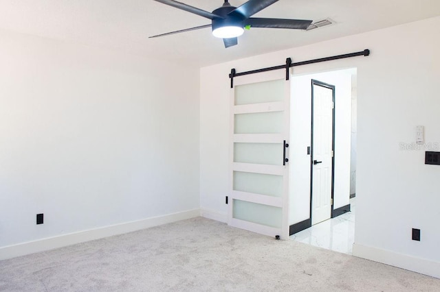 carpeted spare room with a ceiling fan, visible vents, baseboards, and a barn door