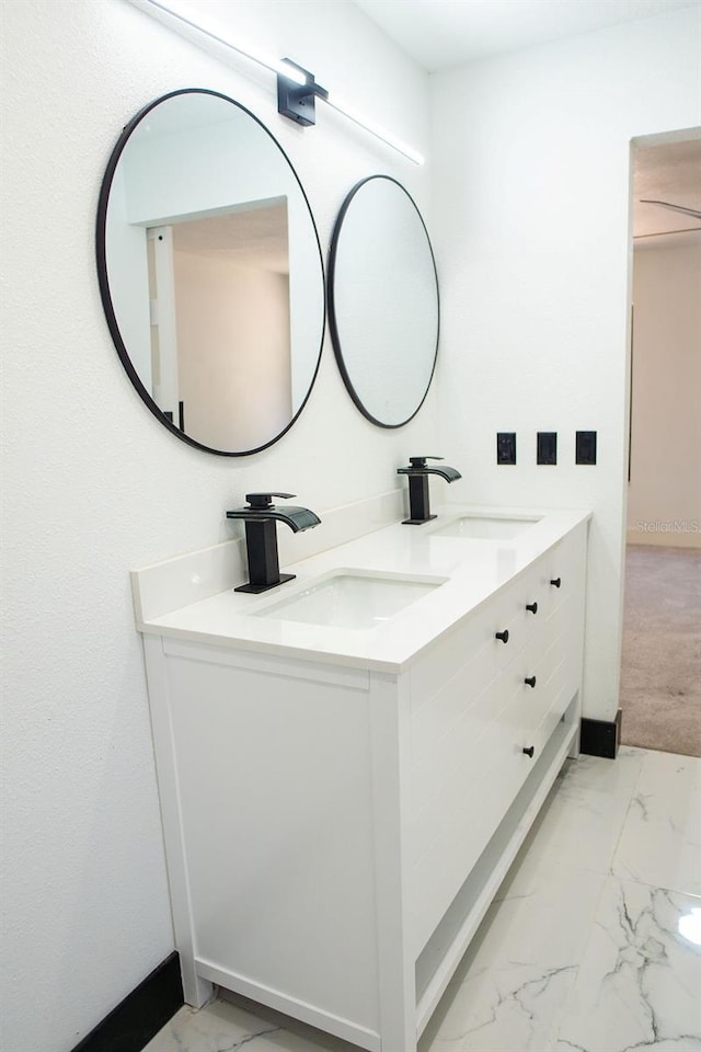 full bathroom with marble finish floor, double vanity, a sink, and baseboards