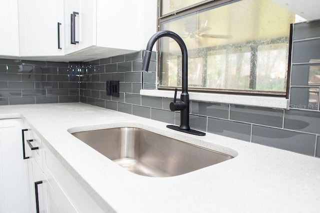 room details with light stone counters, white cabinets, a sink, and backsplash