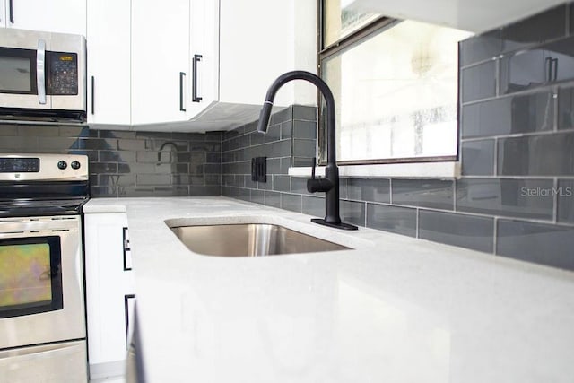 kitchen featuring light stone counters, decorative backsplash, appliances with stainless steel finishes, white cabinetry, and a sink