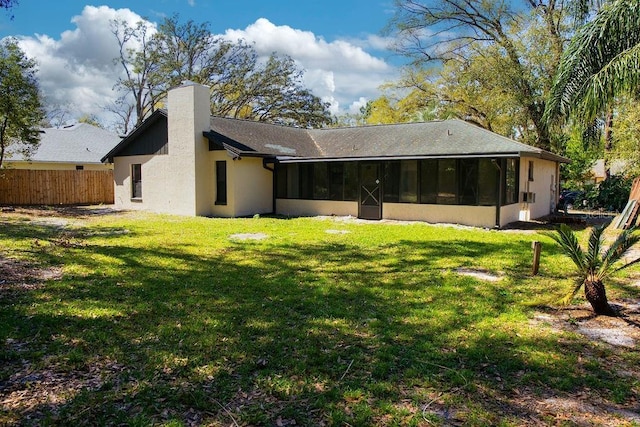 back of property featuring a lawn, a chimney, fence, and a sunroom