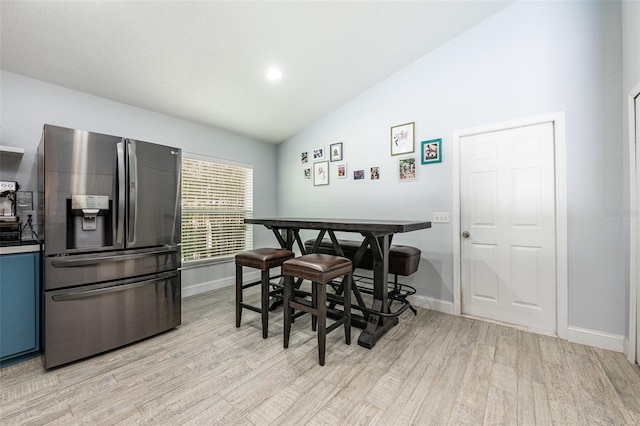 dining room featuring lofted ceiling, light wood-style flooring, and baseboards