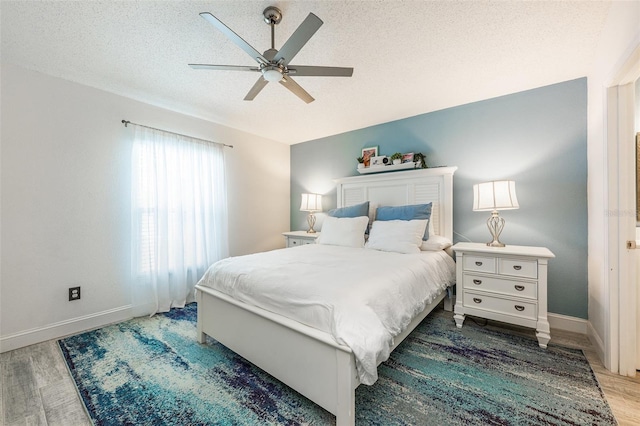 bedroom with light wood finished floors, ceiling fan, baseboards, and a textured ceiling