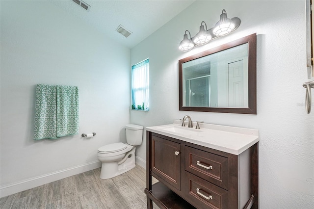 bathroom featuring visible vents, toilet, a shower with shower door, vanity, and wood finished floors