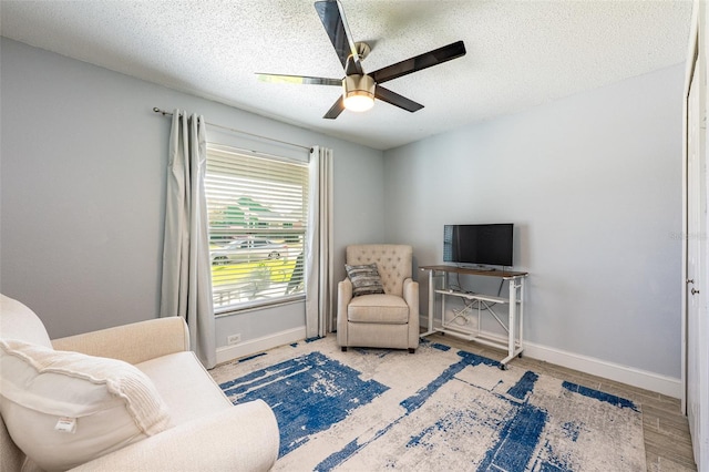 living area with ceiling fan, a textured ceiling, baseboards, and wood finished floors