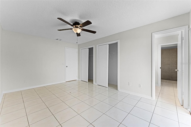 unfurnished bedroom featuring a textured ceiling, light tile patterned flooring, two closets, and visible vents