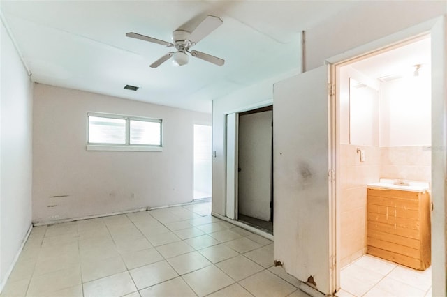 interior space with ceiling fan, light tile patterned flooring, visible vents, and tile walls