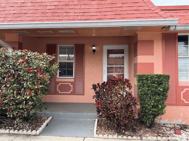 property entrance with a porch, roof with shingles, and stucco siding