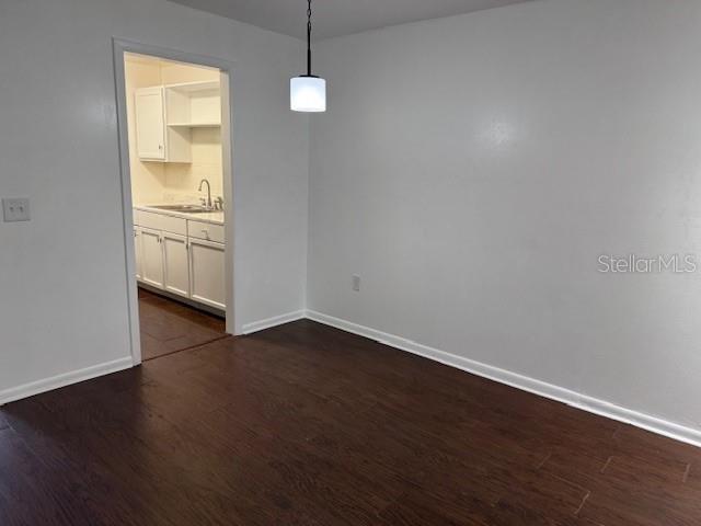 unfurnished dining area featuring dark wood-style flooring, a sink, and baseboards