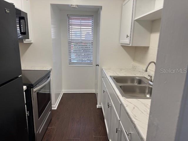 kitchen featuring baseboards, white cabinets, dark wood finished floors, black appliances, and a sink