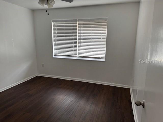 unfurnished room with dark wood-type flooring, a ceiling fan, and baseboards