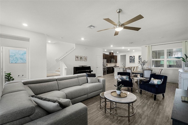 living area with visible vents, ceiling fan, stairway, and wood finished floors