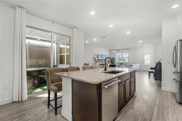 kitchen with light wood-style flooring, dark brown cabinetry, stainless steel appliances, a sink, and open floor plan