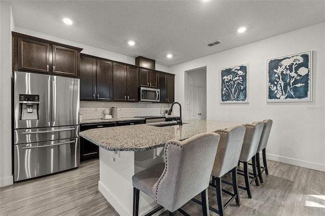 kitchen with a breakfast bar, stainless steel appliances, backsplash, a sink, and light stone countertops