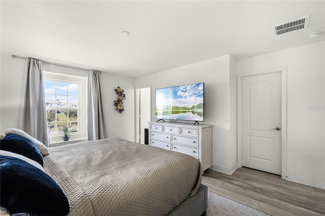 bedroom with light wood-type flooring, baseboards, visible vents, and a textured ceiling