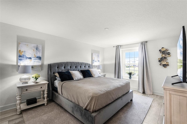 bedroom featuring light wood-style flooring, baseboards, and a textured ceiling