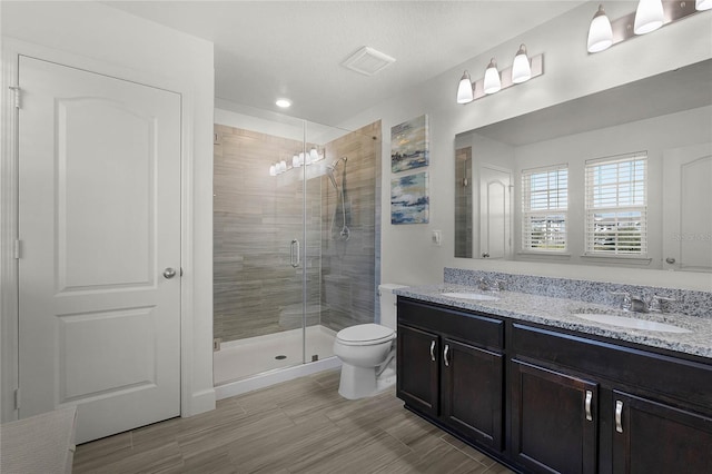 bathroom featuring toilet, a stall shower, double vanity, and a sink