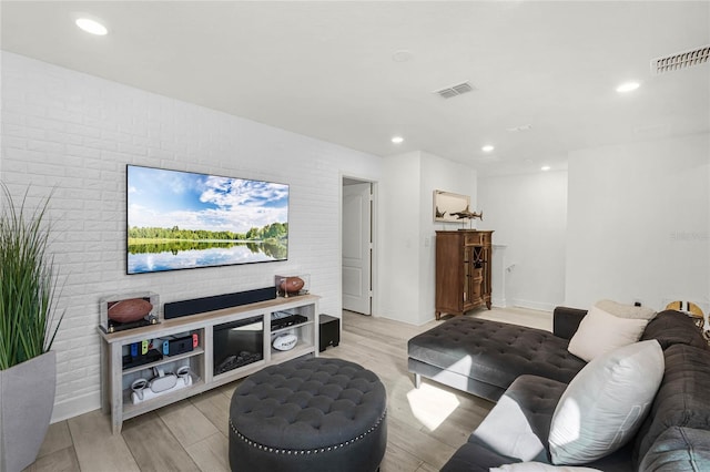 living area featuring brick wall, light wood-style flooring, and visible vents