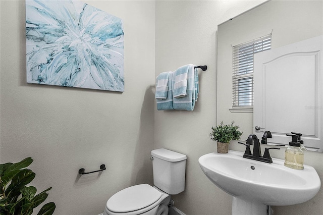 half bath featuring toilet, baseboards, and a sink