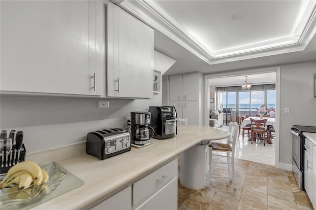 kitchen with a tray ceiling, crown molding, light countertops, electric range, and white cabinetry