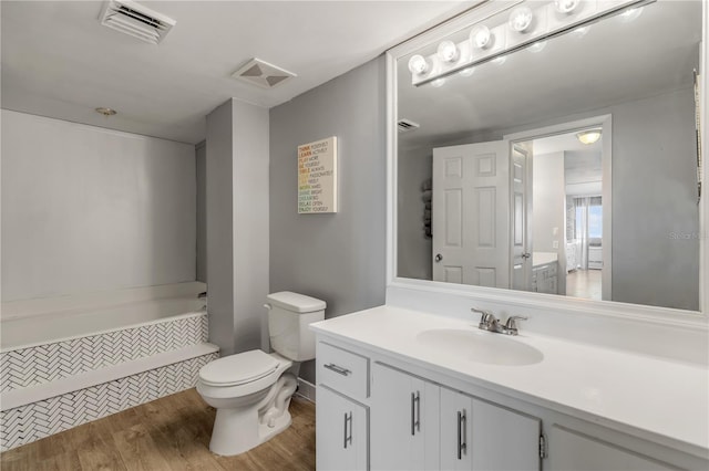 bathroom with visible vents, toilet, wood finished floors, vanity, and tiled tub