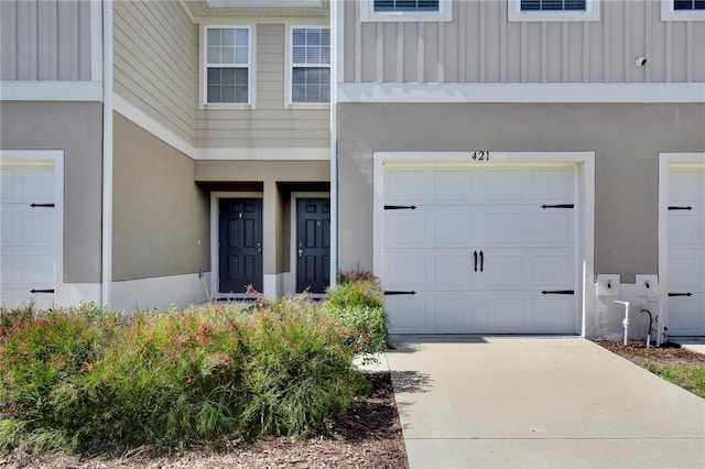 view of exterior entry with board and batten siding, concrete driveway, a garage, and stucco siding