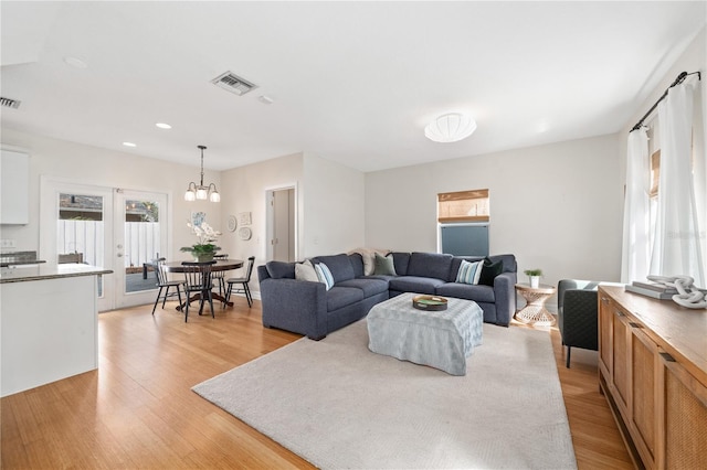 living room with light wood-style flooring, visible vents, and an inviting chandelier