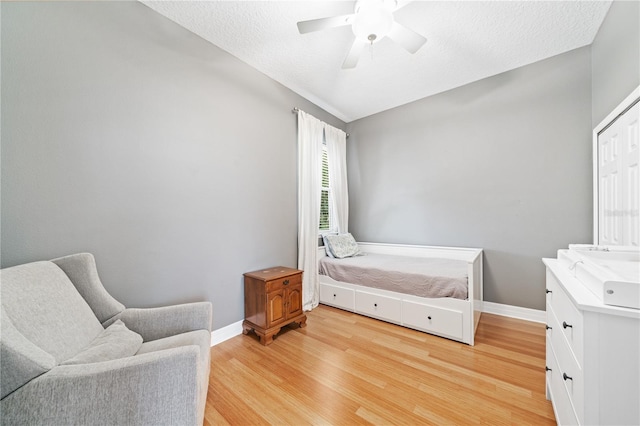 bedroom featuring ceiling fan, a textured ceiling, light wood-style flooring, and baseboards