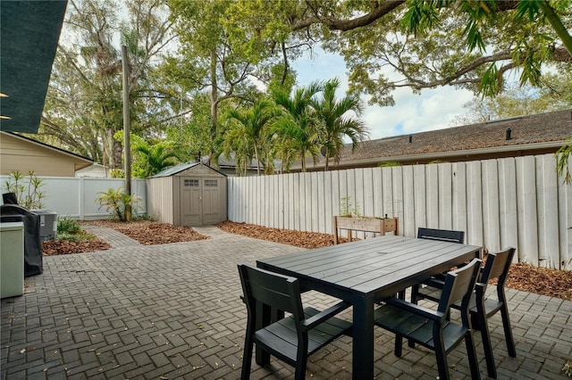 view of patio with an outbuilding, a fenced backyard, outdoor dining space, and a shed