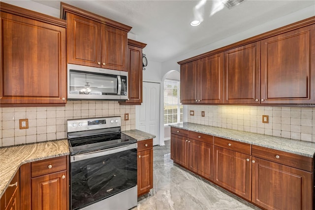 kitchen with arched walkways, marble finish floor, appliances with stainless steel finishes, and light stone countertops