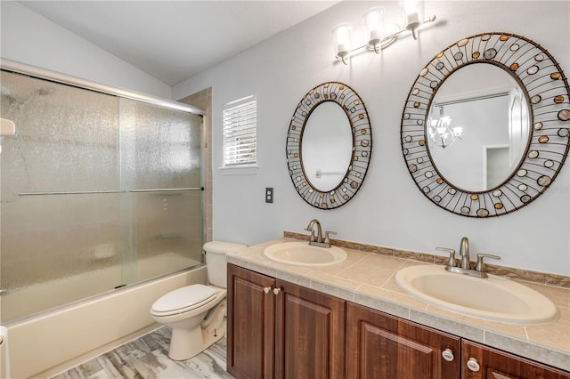 bathroom featuring double vanity, combined bath / shower with glass door, a sink, and toilet