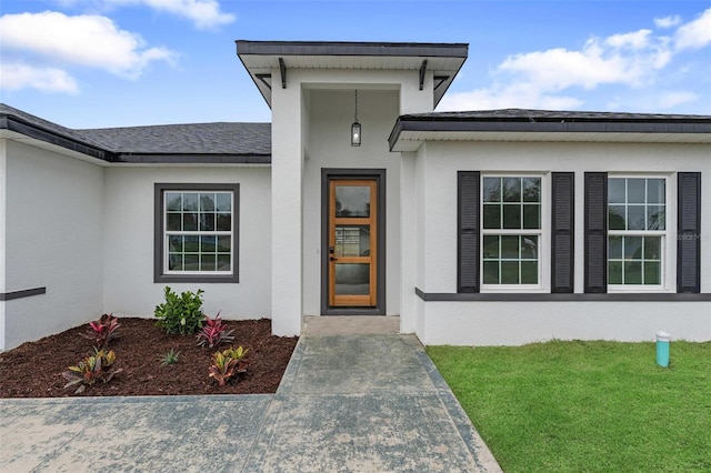 property entrance featuring a yard, a shingled roof, and stucco siding