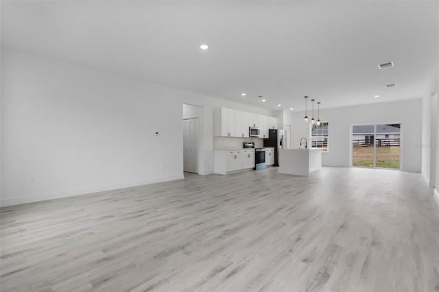 unfurnished living room with light wood-style flooring, a sink, visible vents, and recessed lighting