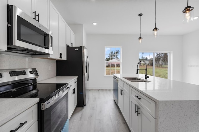 kitchen featuring a center island with sink, stainless steel appliances, decorative backsplash, a sink, and light wood-type flooring