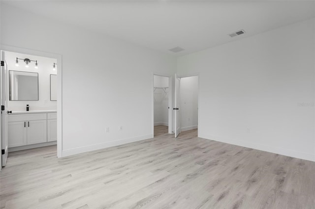 unfurnished bedroom with baseboards, a walk in closet, visible vents, and light wood-style floors