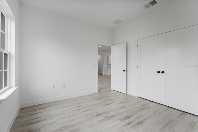 unfurnished bedroom featuring light wood-style floors, a closet, visible vents, and baseboards