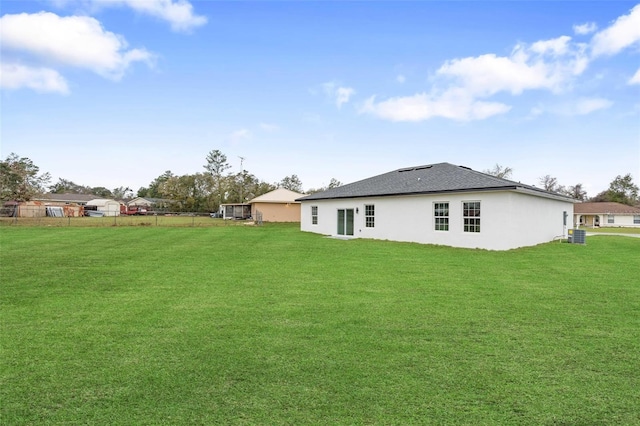 rear view of property featuring roof with shingles, a lawn, fence, and stucco siding