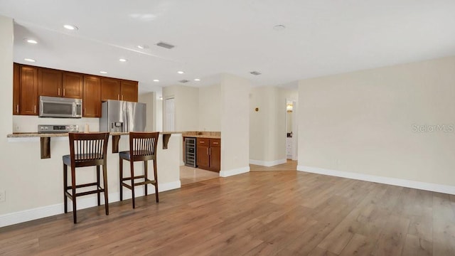 kitchen featuring light wood-style floors, a kitchen bar, wine cooler, and appliances with stainless steel finishes