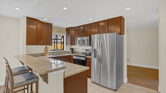 kitchen featuring light tile patterned floors, appliances with stainless steel finishes, a peninsula, light stone countertops, and a kitchen bar