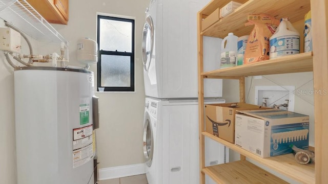 washroom with electric water heater, laundry area, baseboards, stacked washing maching and dryer, and tile patterned floors