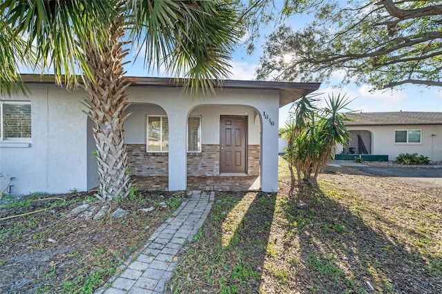 doorway to property featuring a porch, stone siding, and stucco siding