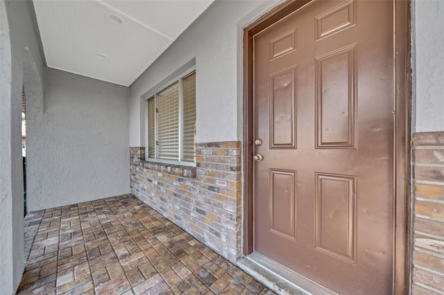 entrance to property featuring brick siding and stucco siding