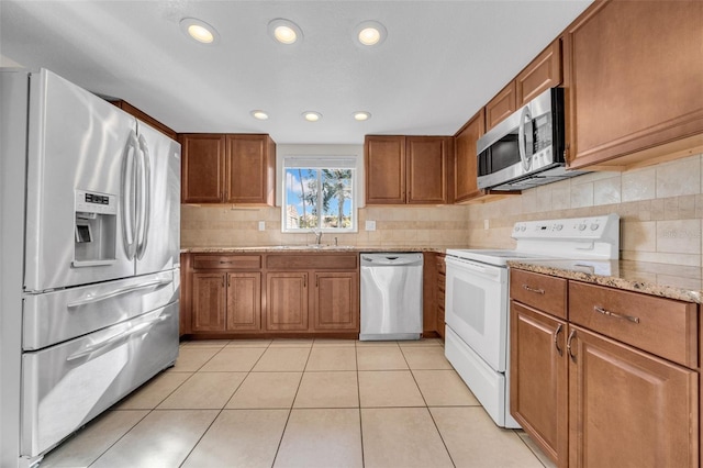 kitchen featuring light tile patterned floors, stainless steel appliances, light stone counters, and brown cabinetry